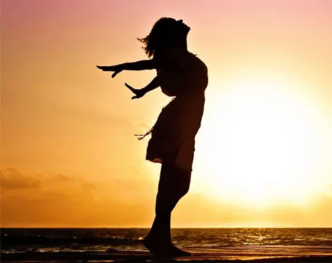 A woman is standing on the beach at sunset.